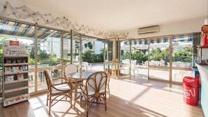 A spacious patio area with a table and chairs, large windows offering a view of the outdoors, and a vending machine. - Hotel Anna (Terracina)