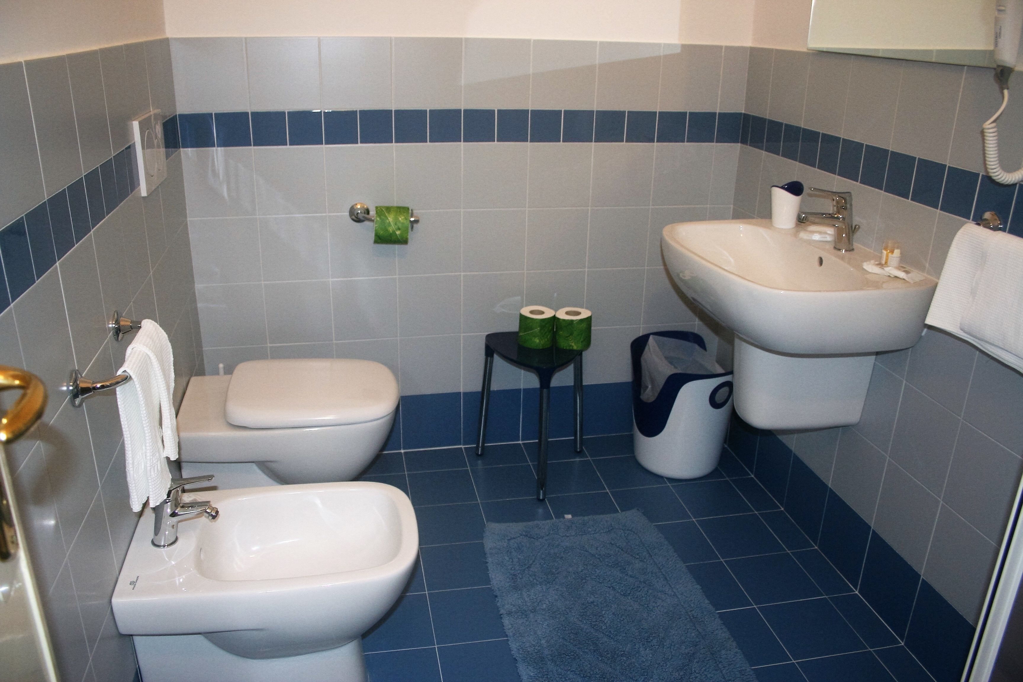 Un baño con inodoro, bidé y lavamanos, paredes con azulejos azules y una alfombra azul.