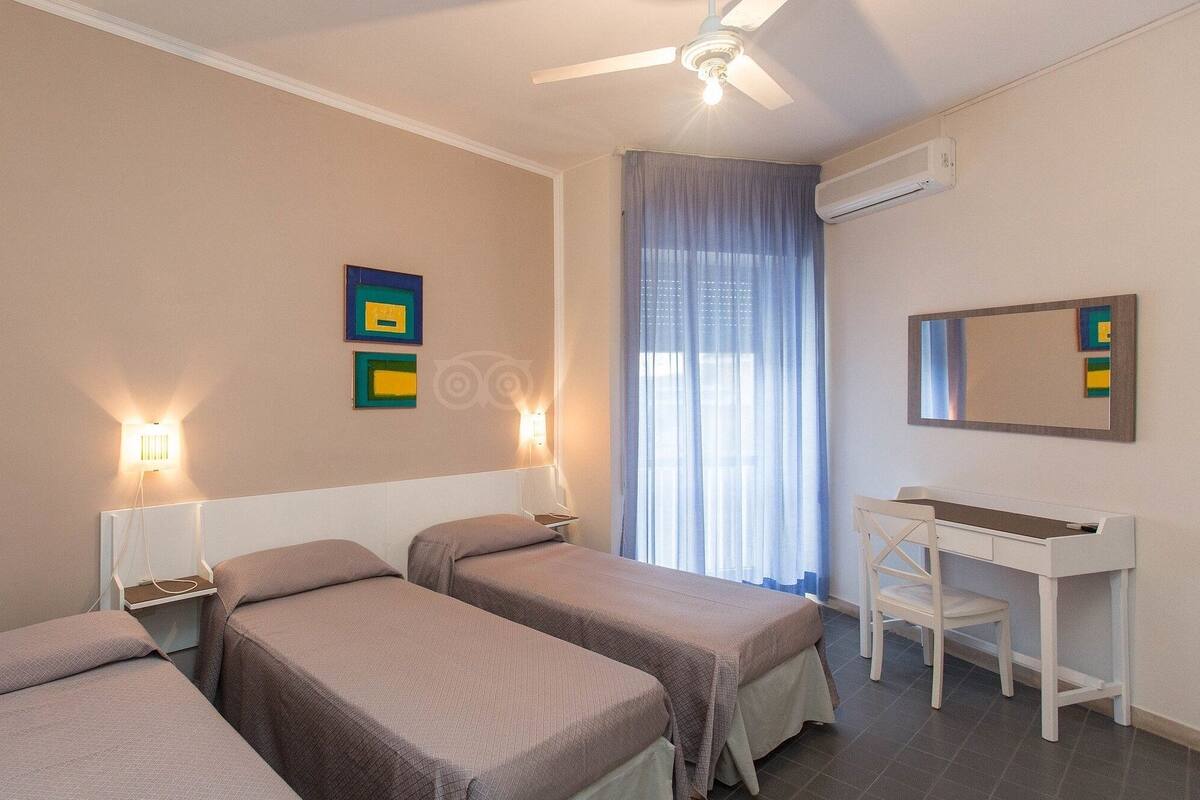 Ein Hotelzimmer mit drei Einzelbetten, einem Schreibtisch und einem Stuhl.