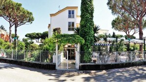 A white building with a gated entrance, surrounded by trees and a fence. - Hotel Anna (Terracina)
