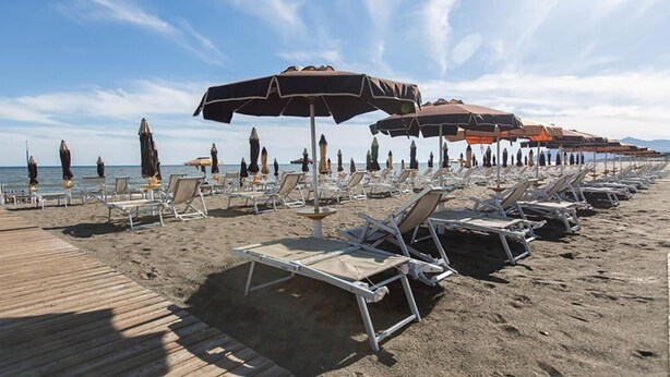 A beach with rows of sun loungers and umbrellas, a wooden boardwalk, and a clear sky. - Hotel Anna (Terracina)