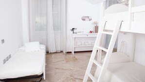 Ein sauberes, weißes Zimmer mit einem Bett, einem Schreibtisch und einer Leiter.