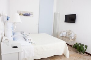 Un dormitorio ordenado con cama, mesita de noche, lámpara y televisor instalado en la pared.