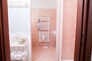 Un baño con estante blanco con toallas, radiador blanco y lavamanos blanco.