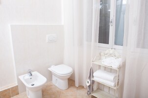 Un bagno con toilette, bidet e uno scaffale con asciugamani.