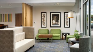 A hotel lobby with a sofa, two armchairs, a coffee table, a lamp, and artwork on the walls. - Holiday Inn Express & Suites Altoona by IHG (Altoona)