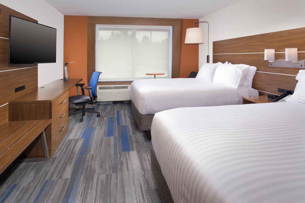 A hotel room with two beds, a desk with a TV, a small table, and a lamp.