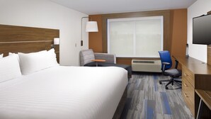 Habitación de hotel con una cama grande, un escritorio con silla, televisión y ventana con vista a la ciudad.