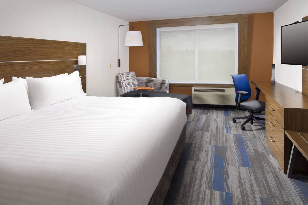 A hotel room with a large bed, a desk with a chair, a television, and a window with a view of the city.