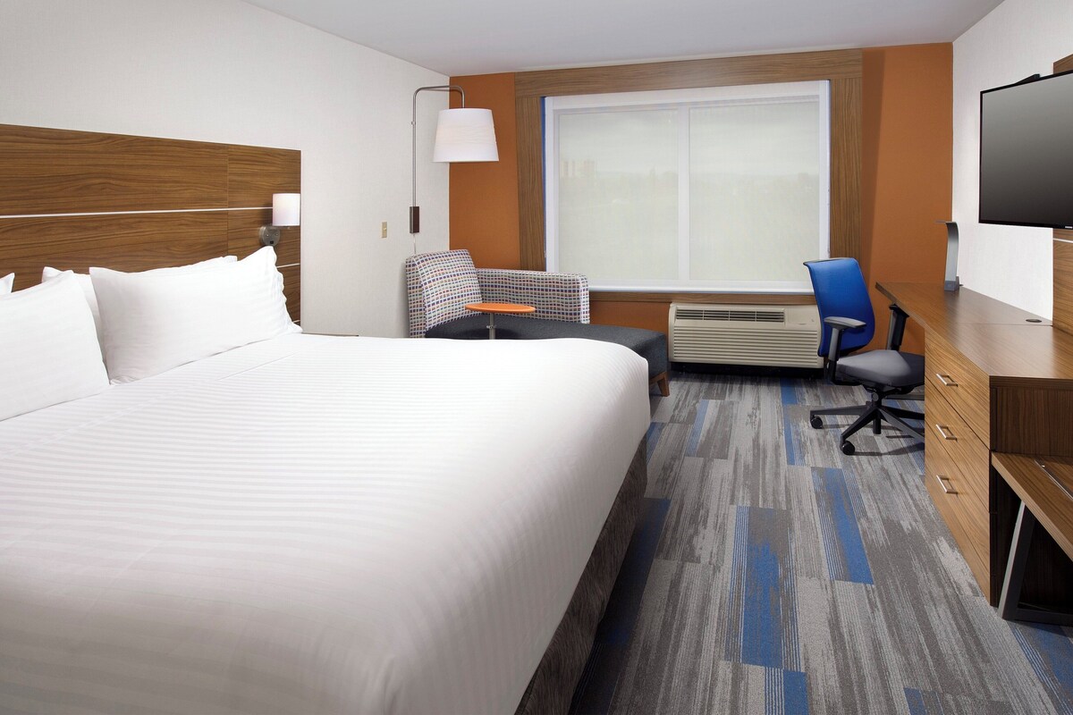 A hotel room with a large bed, a desk, a chair, a television, and a window.