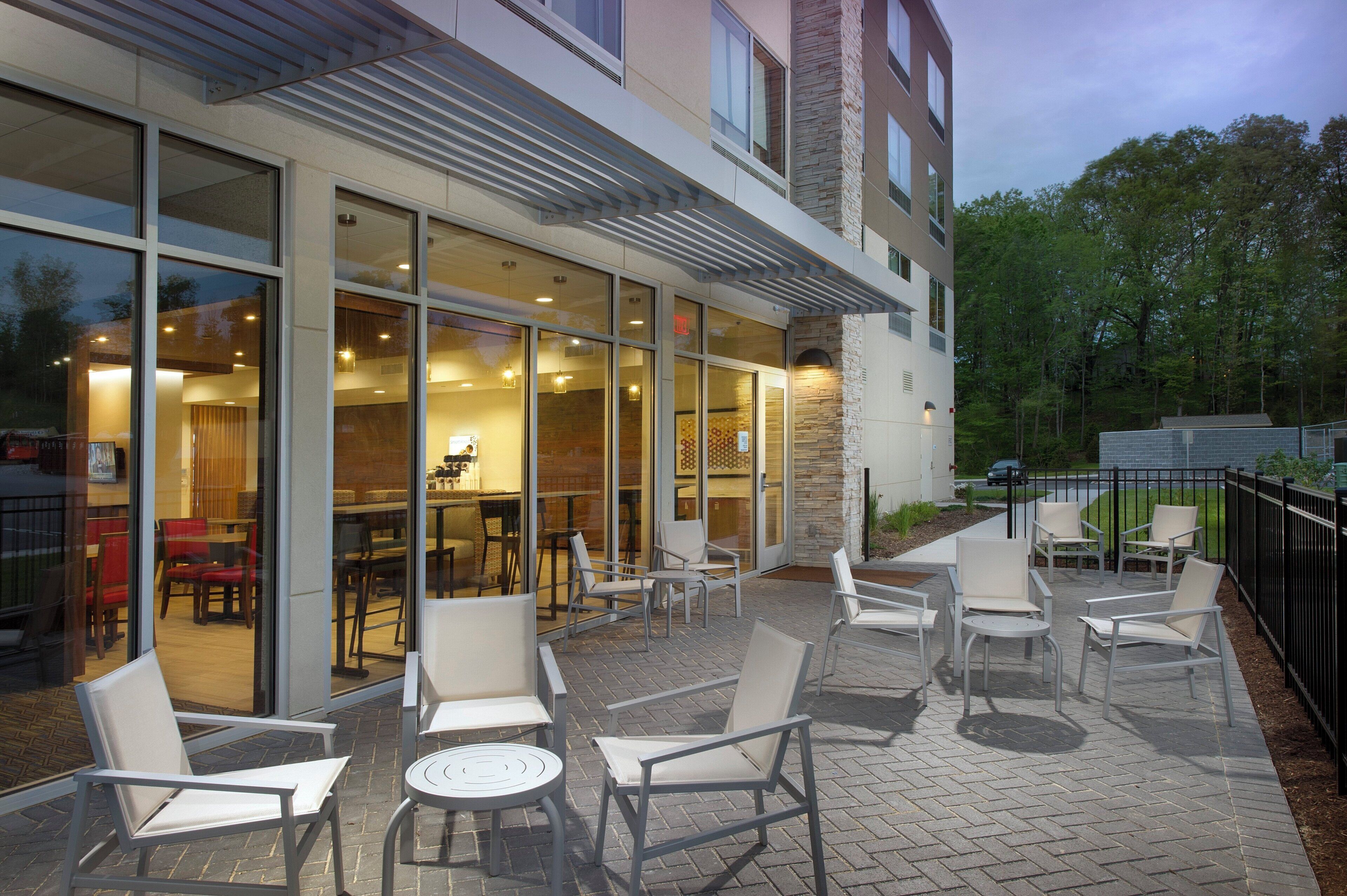 Un espace extérieur aménagé avec des chaises et des tables, un mur en verre et un bâtiment doté d’une façade en pierre.