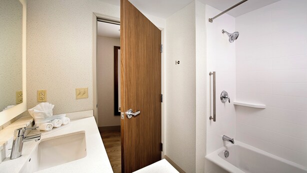 Un baño con lavamanos blanco, puerta de madera, ducha con puerta de cristal y espejo.