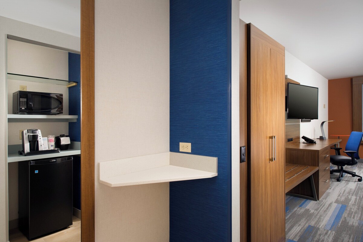 A hotel room with a kitchenette, a flat-screen TV, a desk, and a blue accent wall.