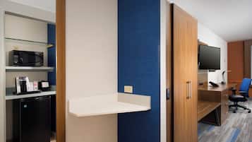 A hotel room with a kitchenette, a flat-screen TV, a desk, and a blue accent wall.