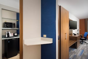 Quarto de hotel com cozinha compacta, TV de tela plana, escrivaninha e parede decorada em azul.