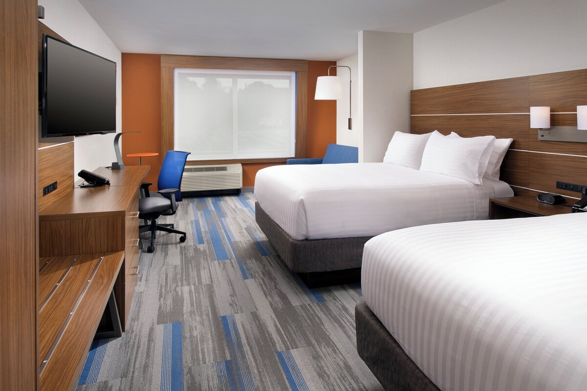 A hotel room with two beds, a desk with a chair, a television, and a window with curtains.