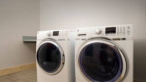 Two front-loading washing machines in a room with wooden flooring and a light-colored wall. - Holiday Inn Express & Suites Altoona by IHG (Altoona)