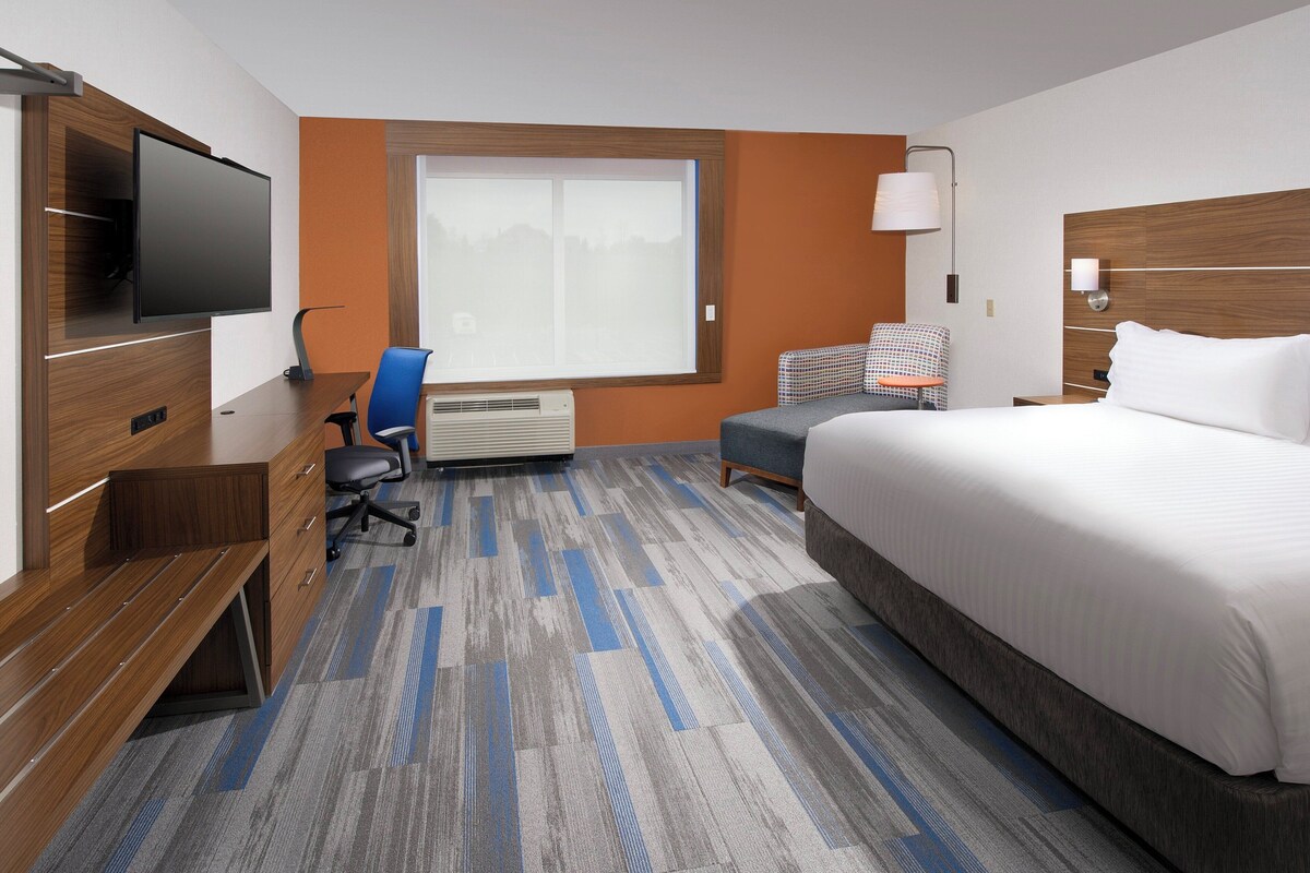 A hotel room with a bed, a desk, a chair, a TV, and a window.