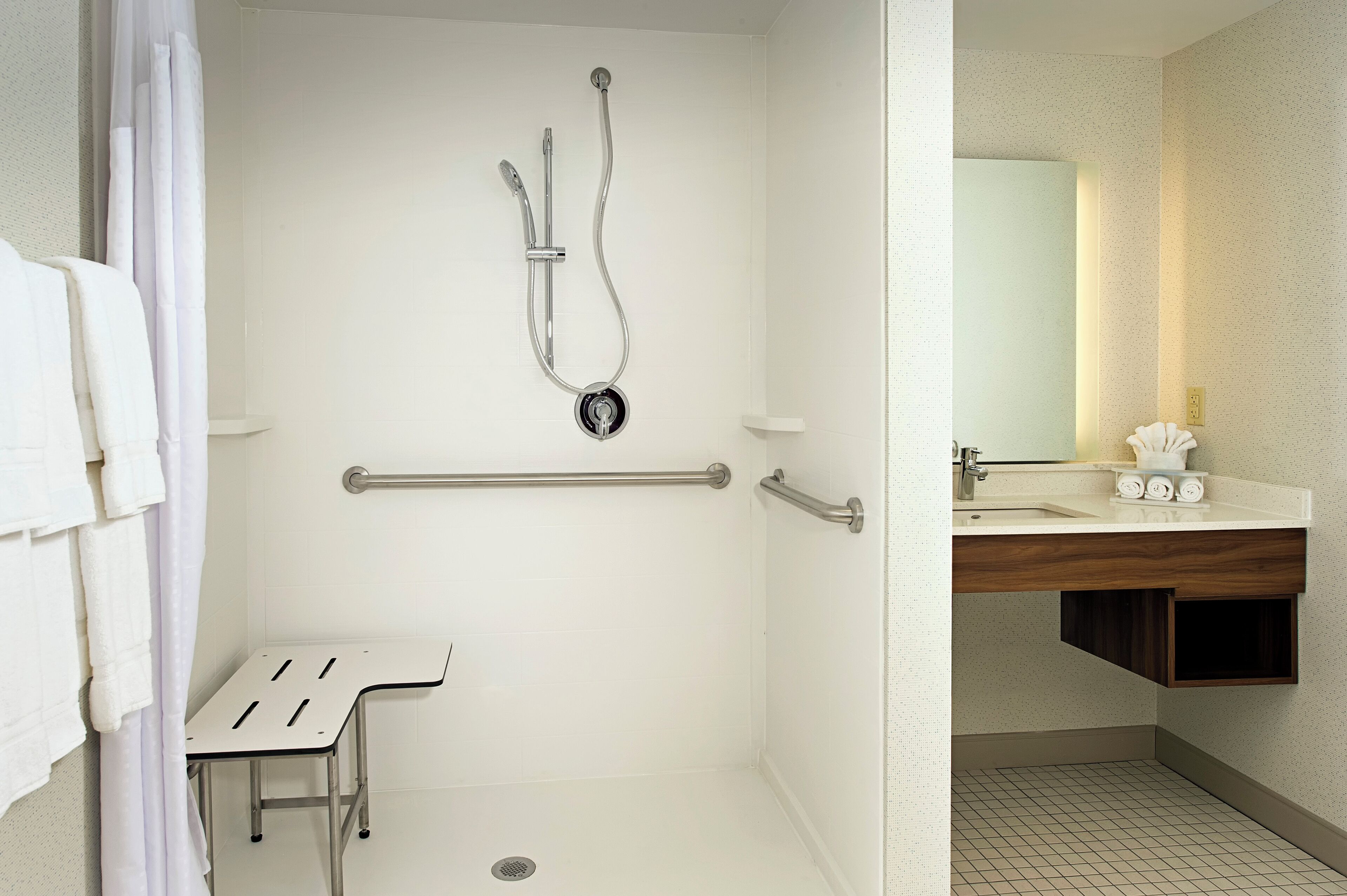 A bathroom with a shower, grab bar, and a sink with a mirror.