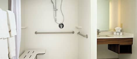 A bathroom with a shower, grab bar, and a sink with a mirror.