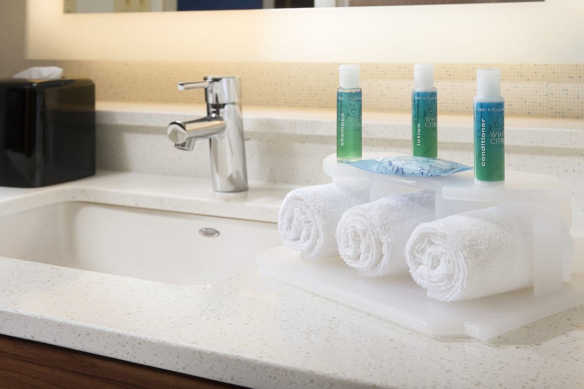 A bathroom sink with a white countertop, a silver faucet, and three bottles of white conditioner and shampoo.