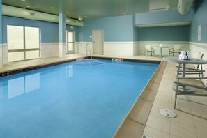 An indoor swimming pool with clear water, a diving board, and a seating area with chairs and a table. - Holiday Inn Express & Suites Altoona by IHG (Altoona)