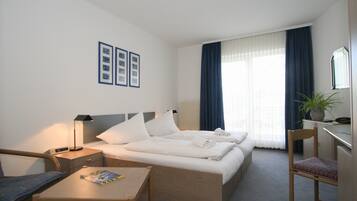 A hotel room with a bed, two bedside tables, a chair, a desk, and a potted plant.