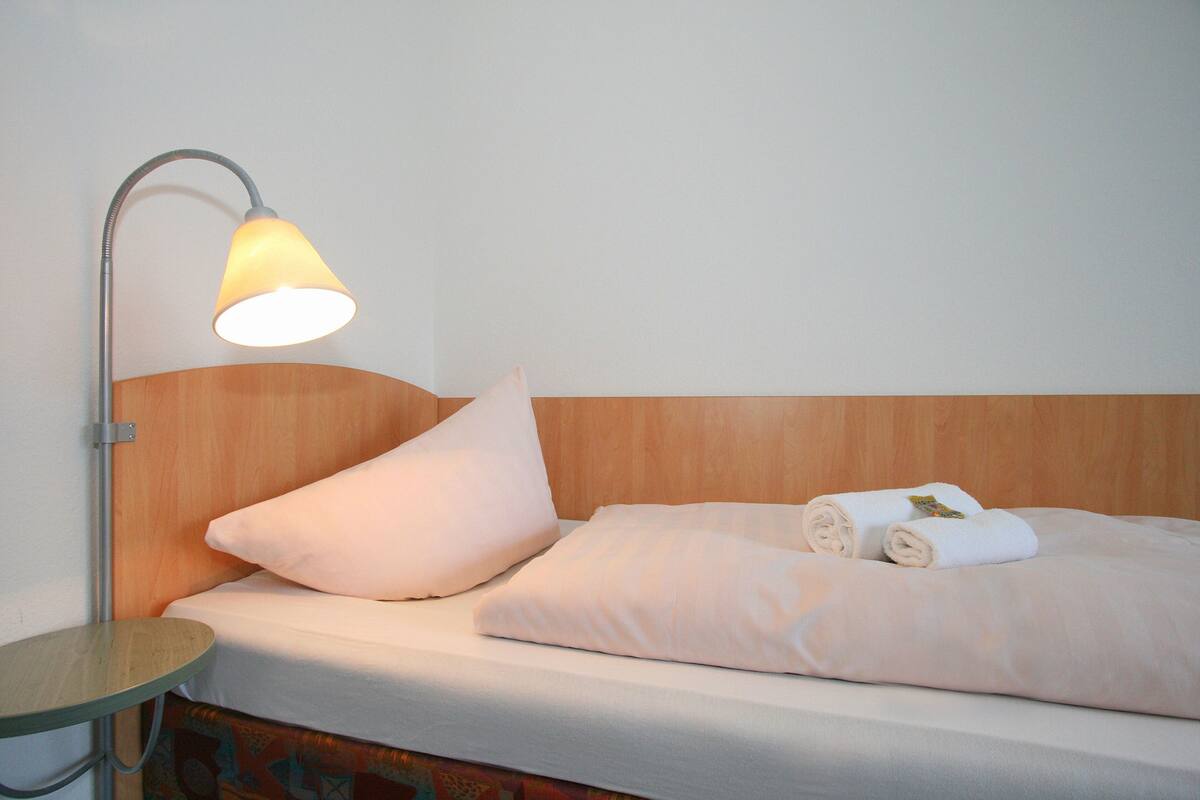 Un lit bien fait, avec un oreiller et des serviettes pliées, une table de chevet et une lampe.