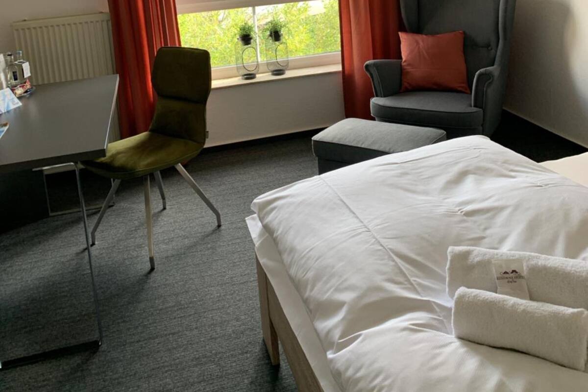 Une chambre d’hôtel avec un lit, deux chaises, une table et une fenêtre avec des rideaux.