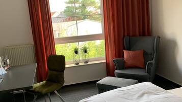 Habitación de hotel con cama, dos sillas, una mesa y un ventanal con cortinas.