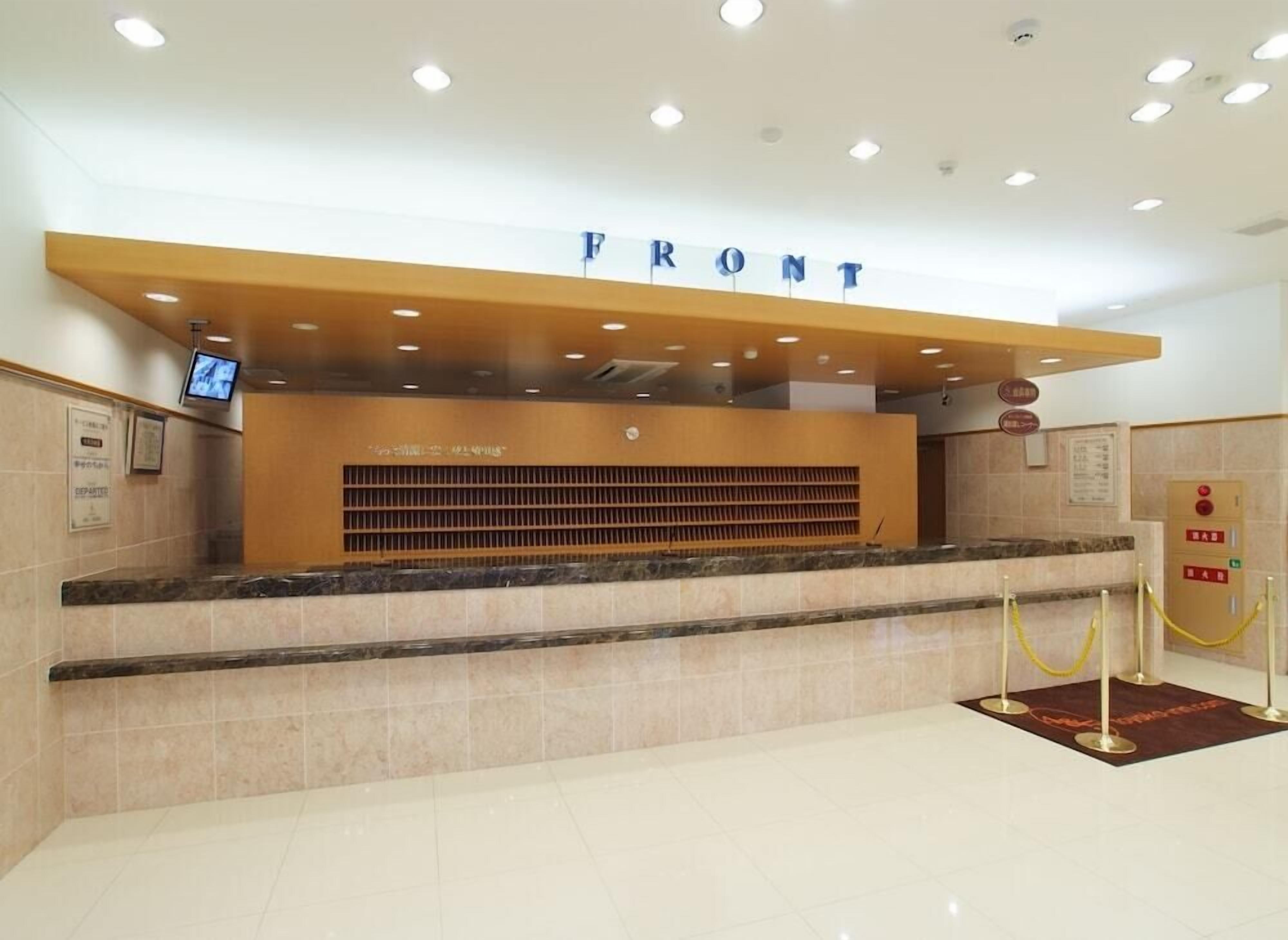 A reception desk with a 'FRONT' sign above it, a digital screen, and a yellow rope barrier.