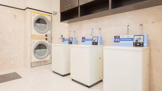 A laundry facility with a front-loading washing machine and three coin-operated dryers. - Toyoko Inn Kumamoto Ekimae (Kumamoto)