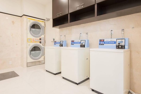 A laundry facility with a front-loading washing machine and three coin-operated dryers. - Toyoko Inn Kumamoto Ekimae (Kumamoto)