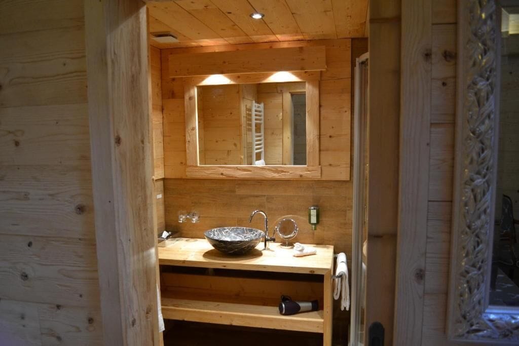 Interior de una cabaña de madera con un lavabo de madera, un espejo y un perchero para toallas.