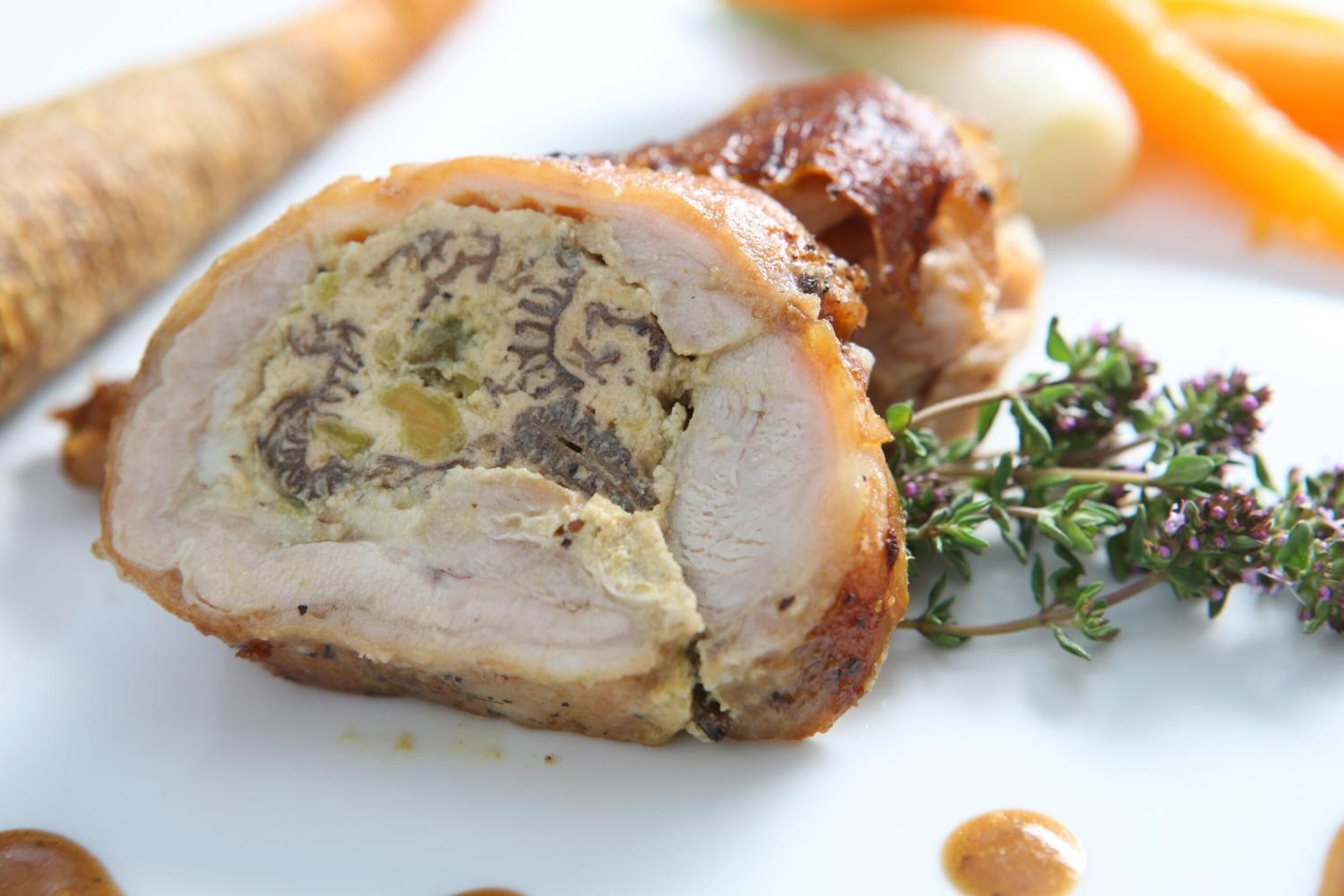 Pechuga de pavo rellena con costra de hierbas, presentada en un plato blanco con adornos de tomillo y acompañamiento de verduras asadas.
