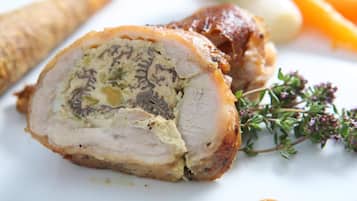 Pechuga de pavo rellena con costra de hierbas, presentada en un plato blanco con adornos de tomillo y acompañamiento de verduras asadas.