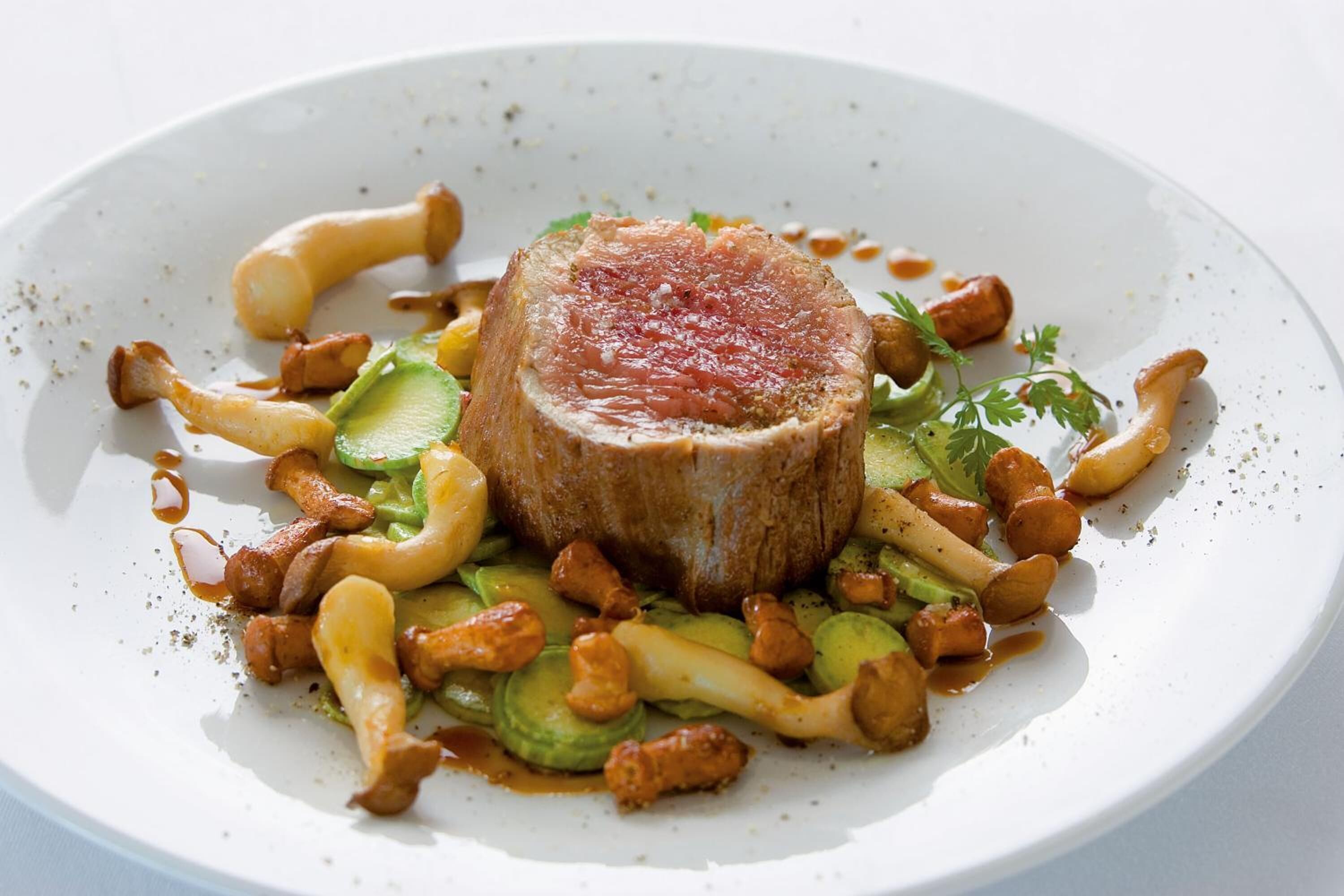 A plate of food with a central piece of meat, surrounded by vegetables and mushrooms.