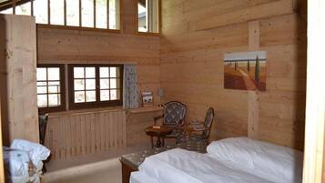 Una stanza di una baita di legno con un letto, una sedia, un tavolo e una finestra.