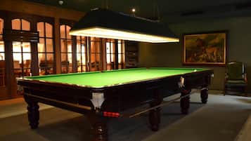 Une table de billard dans une pièce dotée d’une grande fenêtre, d’un tableau au mur et d’une chaise.