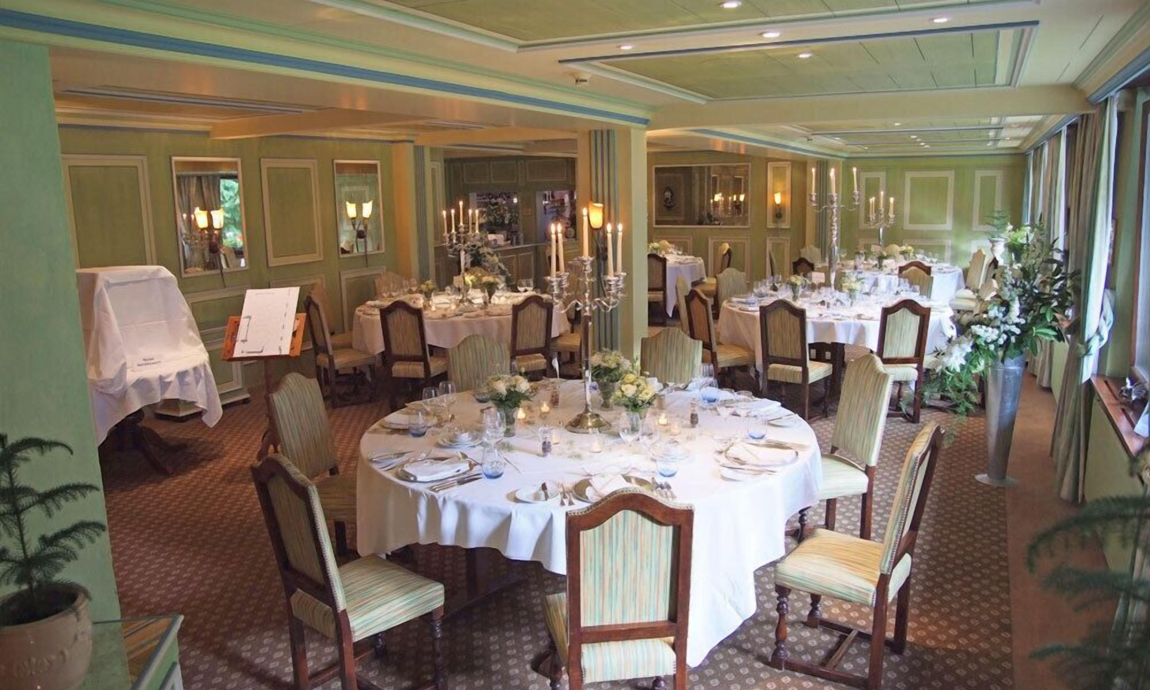 Un comedor formal con mesas redondas dispuestas para varios invitados, con manteles blancos, sillas y centros de mesa con flores.