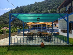 Un patio exterior con mesas y sillas, un espacio de estar techado y una piscina.