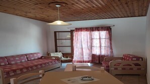 Una habitació acollidora amb sostre de fusta, un sofà, una cadira, una taula i una finestra amb cortines.