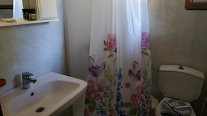 Un bany amb un rentapeus blanc, un vàter i una cortina de bany amb motius florals.