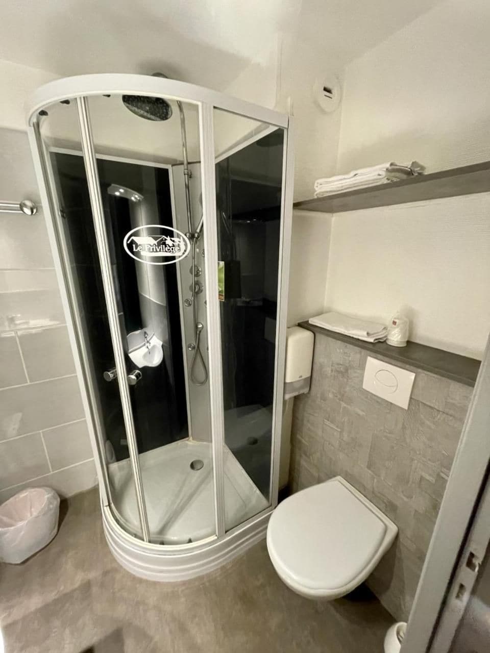 Un baño moderno con ducha envuelta en vidrio, inodoro blanco y dispensador de toallas.