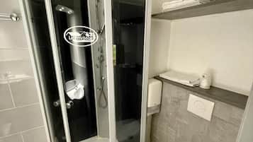 Un baño moderno con ducha envuelta en vidrio, inodoro blanco y dispensador de toallas.