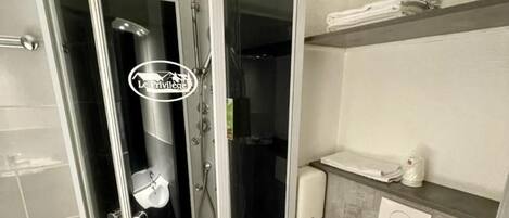 Un baño moderno con ducha envuelta en vidrio, inodoro blanco y dispensador de toallas.