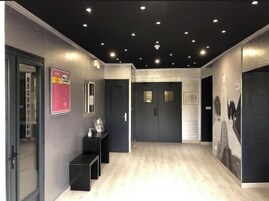 Uma área de recepção de hotel com design moderno, com balcão de atendimento, painel digital e sinalização na parede.