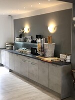 Uma cozinha moderna com armários cinzentos, máquina de café embutida e bancada com diversos utensílios de cozinha.