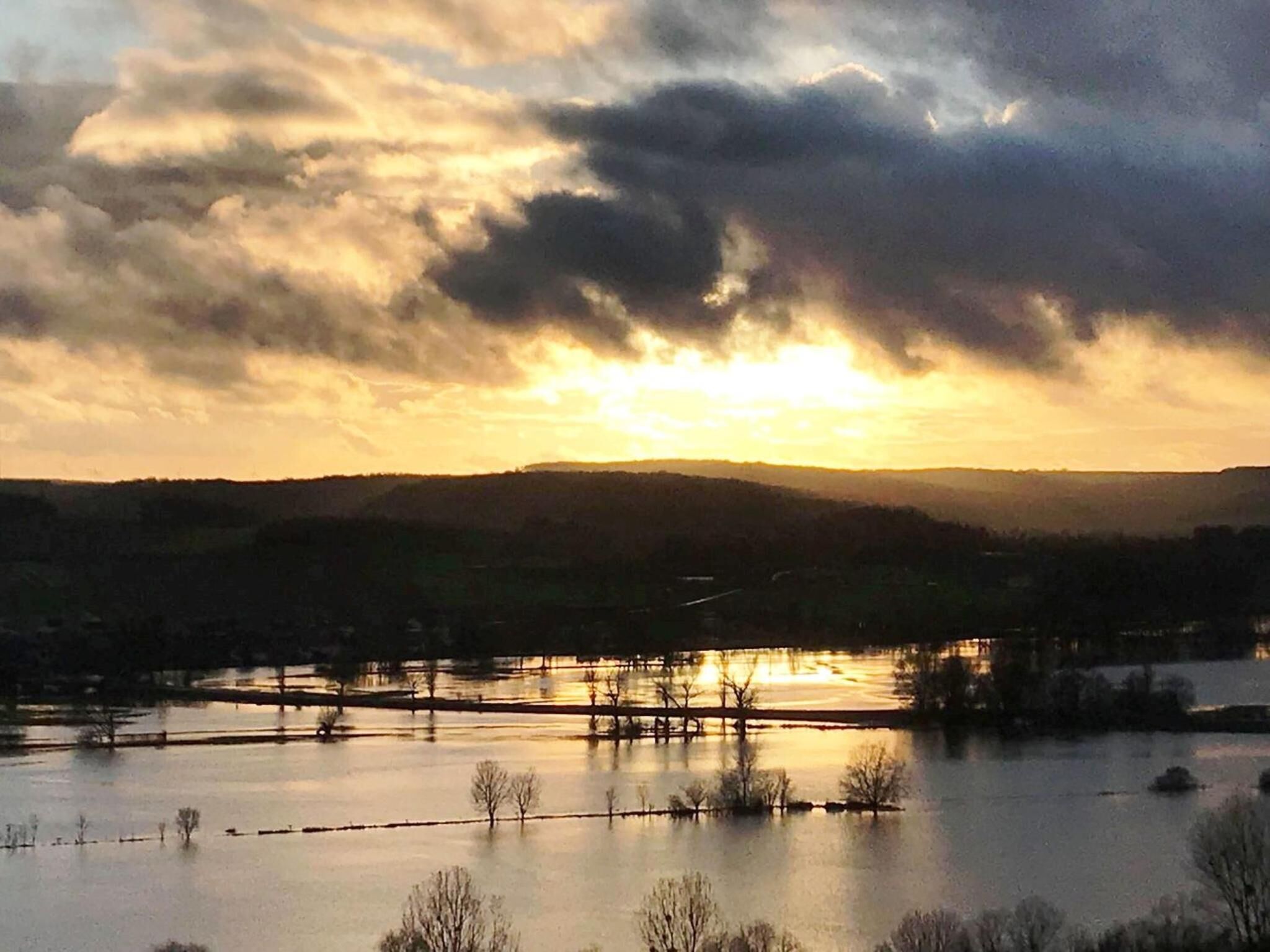 A sunset over a river with a bridge and distant hills.