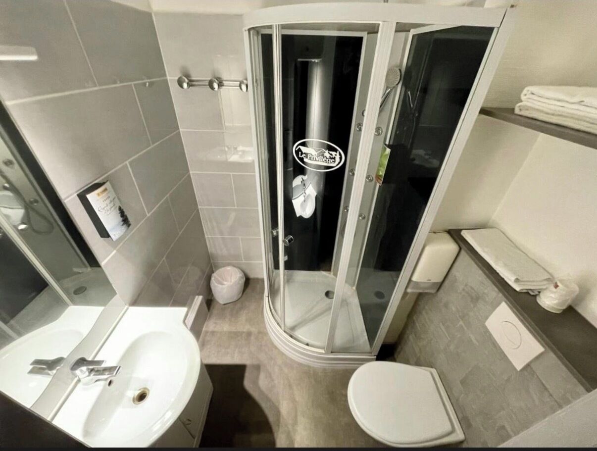 Un bany modern amb dutxa envidrada amb vidre, un lavabo blanc i un vàter.